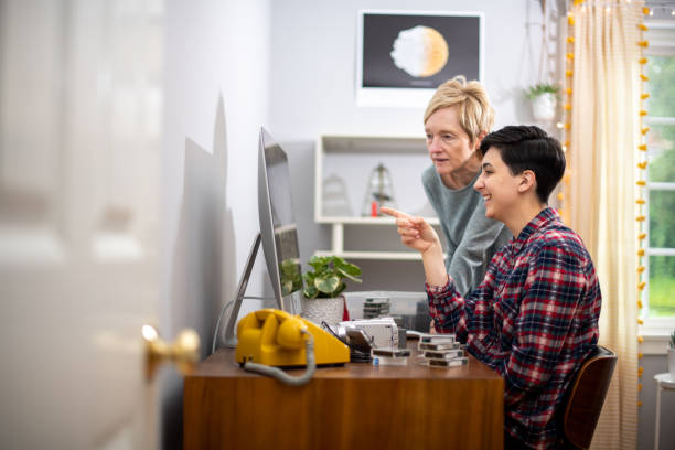 Mother Looks at her Daughter's Video Editing Job as she Works Woman edits home movies in her home office during the coronavirus pandemic. Her mom stands next to her as she shares some of the funny moments from their trips. female film editor stock pictures, royalty-free photos & images