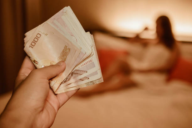 istock Abstract of someone hand holding Thai bath money with blurred background image (defocus) of Prostitution woman sitting on the bed in hotel. 1218123440