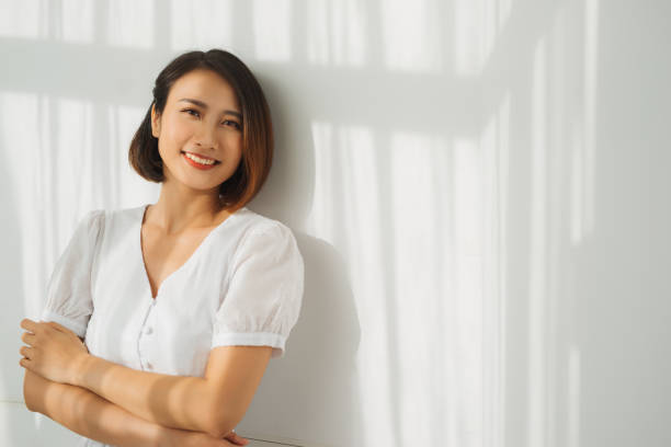 istock A young beautiful is standing against the wall, the sunlight is beautifully falling. Shade from the blinds. 1218126018