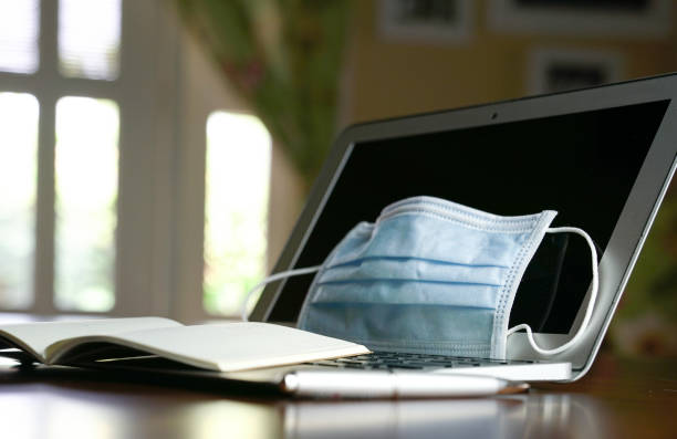 istock Medical face mask on on top of computer laptop on table 1218126821