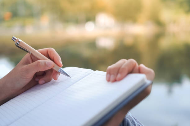 istock Woman hand writing down in small white memo notebook for take a note not to forget or to do list plan for future. 1218128320