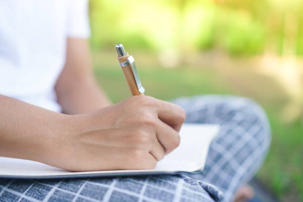 istock Woman hand writing down in small white memo notebook for take a note not to forget or to do list plan for future. 1218128332
