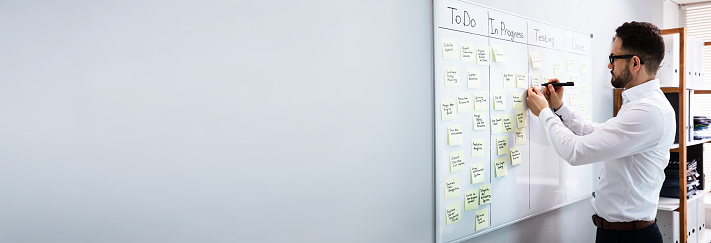 Side View Of Businessman Writing On Sticky Notes Attached To White Board In Office