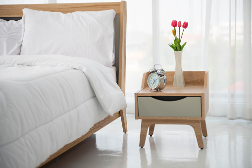 Close up of modern bed and bedside cabinet with clock and flower vase in the bedroom