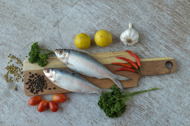 Delicious fresh fish with aromatic herbs, spices and vegetables isolated on white texture wooden table with top view