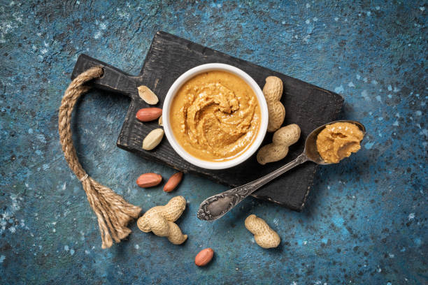 istock Tasty peanut paste in white bowl and vintage spoon with raw nuts 1218145895