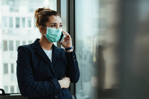 istock Businesswoman with protective mask talking on mobile phone by the window. 1218148152