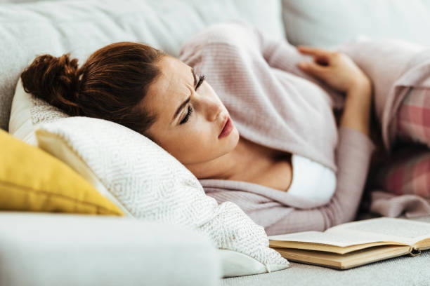 istock Young woman with stomachache lying down on sofa at home. 1218148852
