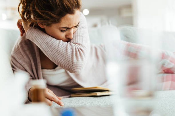 istock Sick woman sneezing into her elbow while lying down on sofa at home. 1218149295