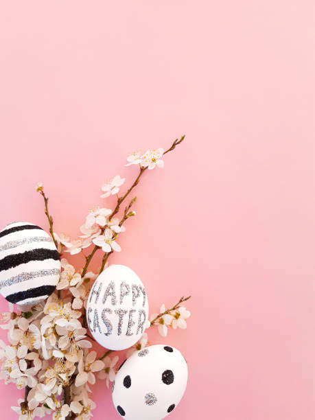 istock Composition of spring flowers, blooming tree branches and eggs with black, silver lines and polka dots on a pink background. Glitter inscription Happy Easter. Flat lay, top view, close up, copy space 1218149485