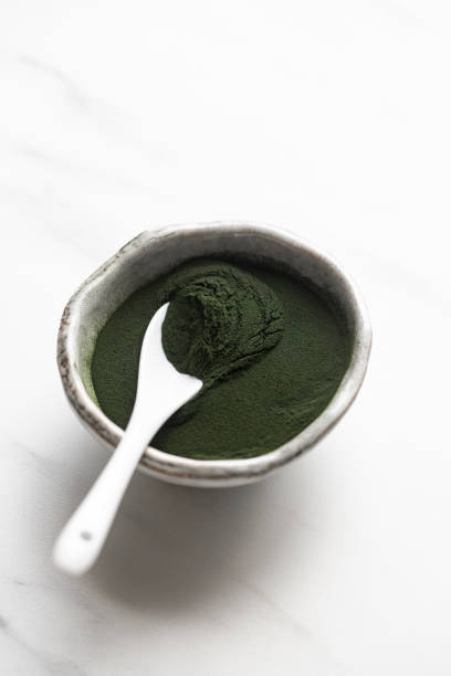 Organic spirulina powder in rustic bowl on white marble background
