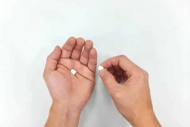 Photo of Half white medicine pill on hand palm. Decrease in dosage due to high price.