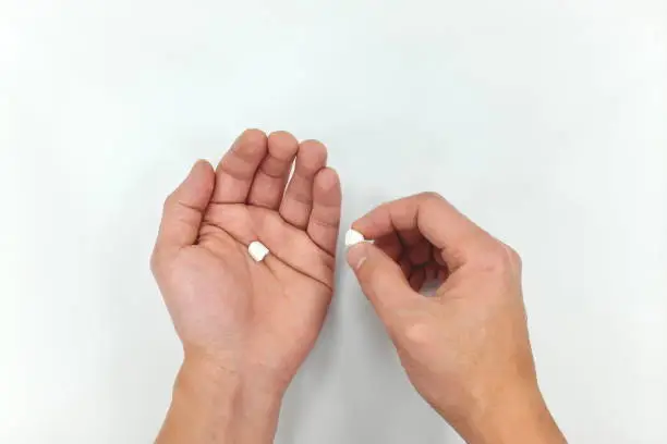 Half white medicine pill on hand palm. Decrease in dosage due to high price.