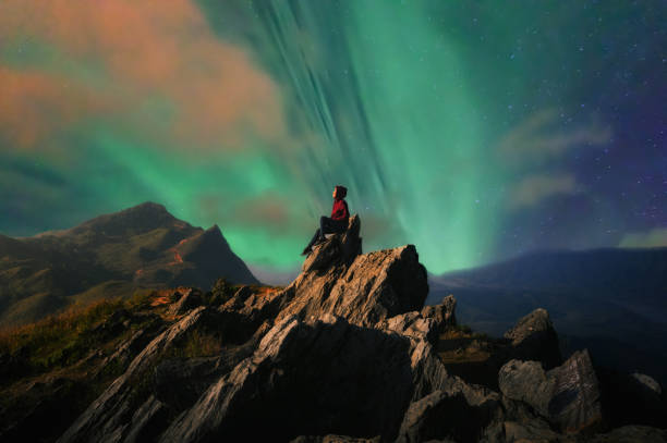 Woman on top Women tourists sit at the top of the rock with Northern Lights or Aurora Borealis, Beautiful landscape. superhero environment women green color stock pictures, royalty-free photos & images