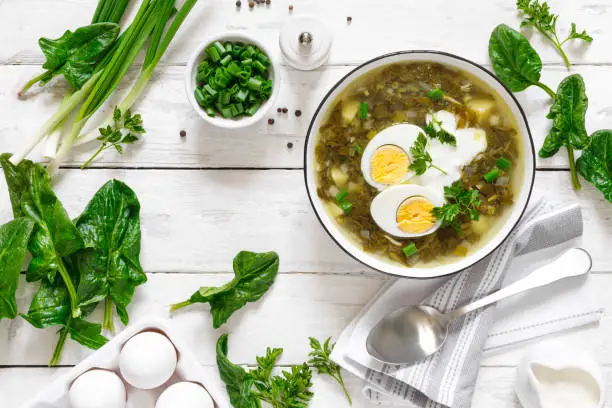 Green sorrel and spinach soup with boiled egg and sour cream on white wooden rustic table, top view