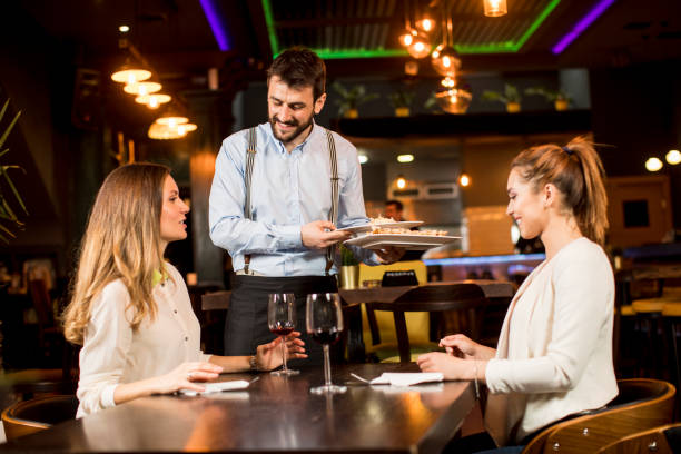 istock Smiling young female friends at a restaurant with waiter serving dinner 1218168045