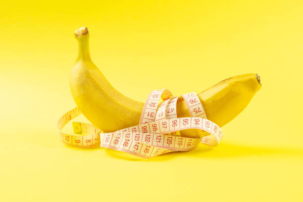 istock Banana with tape for measuring figure. Centimeter ruler spinned around fruit. Tape wrapped around banana isolated on yellow background. Weight loss, healthy food and slim body concept 1218172901