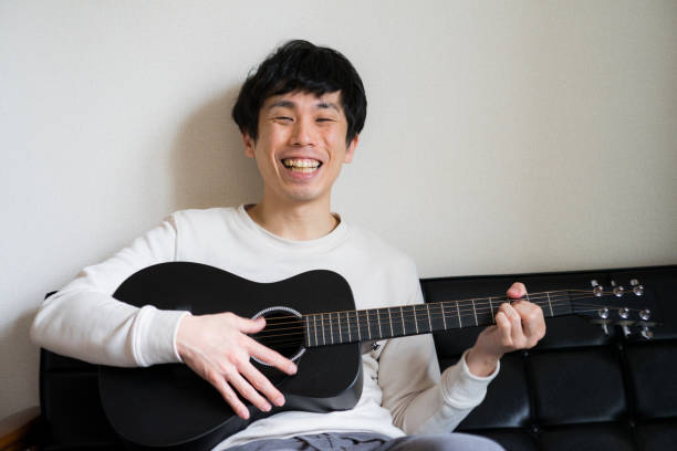 istock Young man sitting on sofa and playing guitar at home. 1218176356