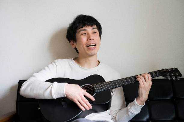 istock Young man sitting on sofa and playing guitar at home. 1218176357
