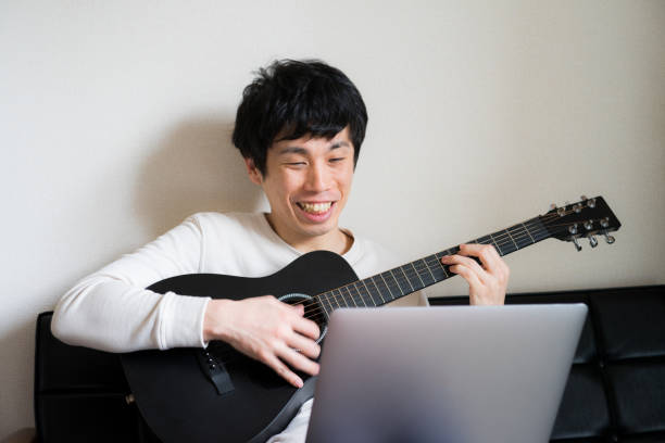 Young man sitting on sofa and playing guitar at home.