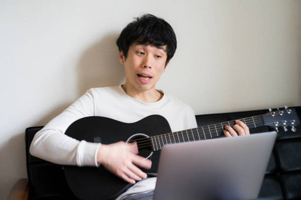 istock Young man sitting on sofa and playing guitar at home. 1218176365