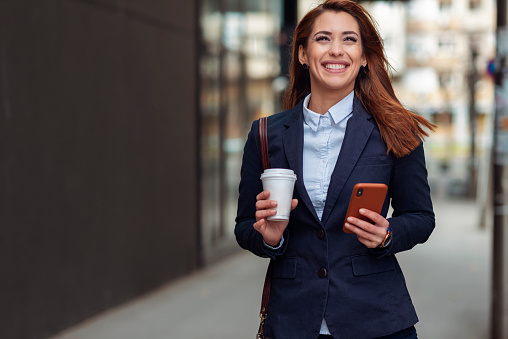 Beautiful business woman walking outdoor.Holding coffee for go and phone.