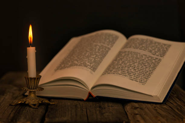 istock Open Torah and a burning candle in a candlestick on a wooden surface on a dark background 1218186920