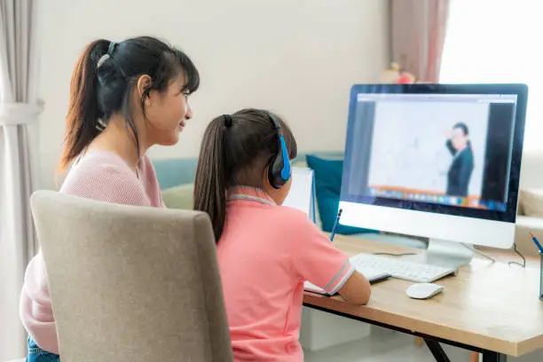 Asian girl student with mother video conference e-learning with teacher on computer in living room at home. Homeschooling and distance learning ,online ,education and internet.