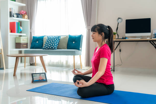 istock Asian woman making yoga exercise for step away from their computers to take mid-day exercise breaks via livestream videos classes on digital tablets during working from home. 1218190244