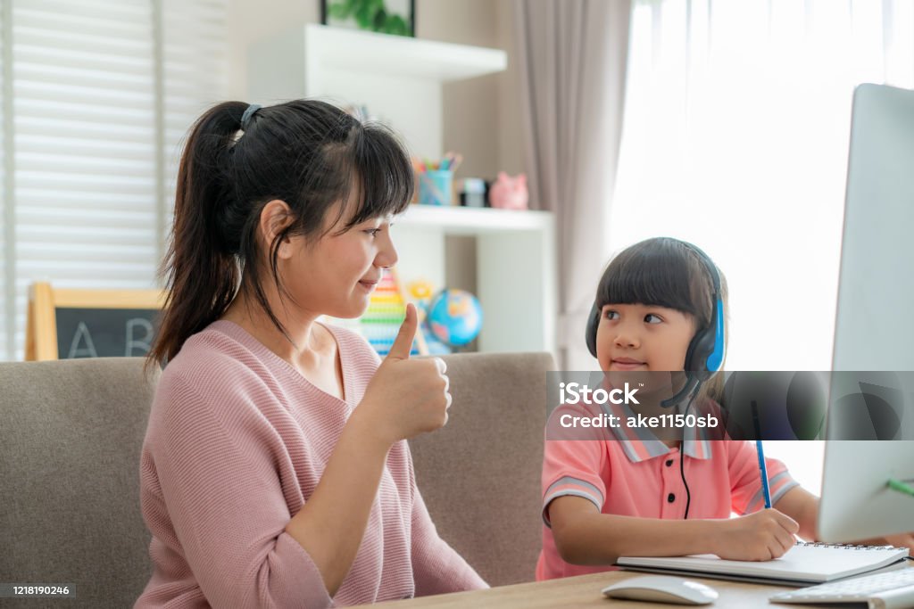 Asian girl student with mother thumb up to her daughter while video conference e-learning with teacher on computer in living room at home. Homeschooling and distance learning ,online ,education and internet. Thumbs Up Stock Photo
