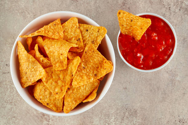Mexican nachos or tortilla chips in a bowl with one nachos is dipped into chili salsa sauce Mexican nachos or tortilla chips in a bowl with one nachos is dipped into chili salsa sauce. Macro top view. tortilla chip photos stock pictures, royalty-free photos & images
