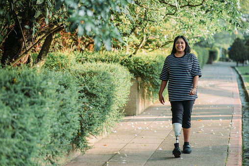 Indigente asiática discapacitada con pierna protésica sonriendo mujer trotando y haciendo ejercicio en el parque público en el día soleado photo
