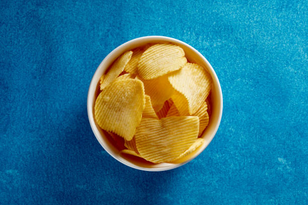istock Crispy potato chips in a white bowl on blue background 1218192910