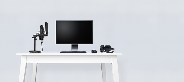 Image representing white table mockup with desktop computer and sound recording equipment: microphone and headphones