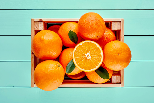 Fresh oranges in a wooden box or crate on  blue wooden table. Top view.