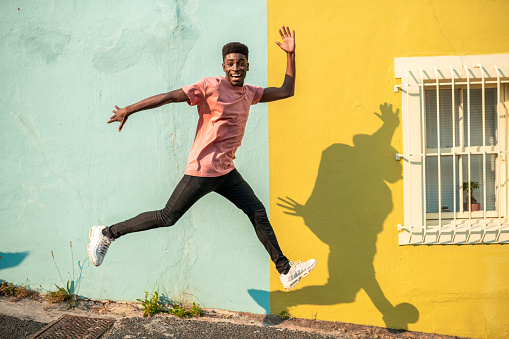 Young man jumping on the street. He has light blue wall as a background