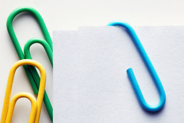 Colorful plastic paper clips attached to a blank white paper. Close up view.