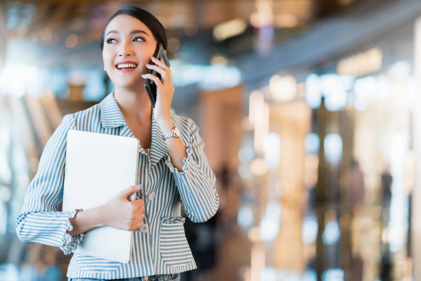 unternehmer-startup-geschäftsinhaber attraktive asiatische geschäftsfrau kommunikation mit smartphone und laptop weißes kleid fröhlich und lächeln mit konfizigkeit verschwommen büro hintergrund - retail shopping talking customer stock-fotos und bilder