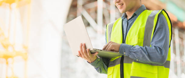 istock smart asian male professional civil engineer hand hold laptop site construction check with infastrcture and building background 1218202565