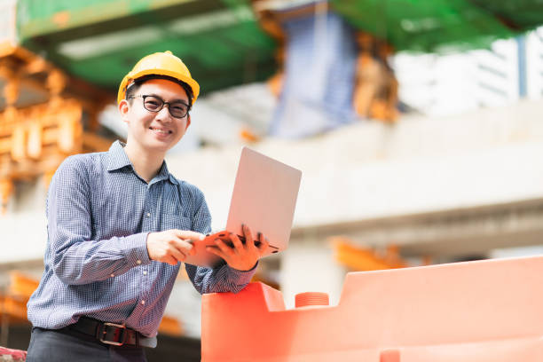 istock smart asian male professional civil engineer hand hold laptop site construction check with infastrcture and building background 1218202580
