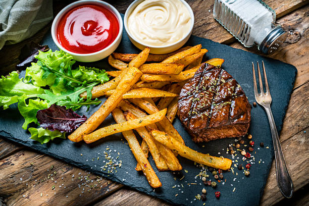 Grilled tenderloin with French fries and salad Grilled tenderloin with French fries and salad served on a slate board. Two bowls with ketchup and mayonnaise are at the top of an horizontal frame. A salt shaker complete the composition. High angle view. High resolution 42Mp studio digital capture taken with SONY A7rII and Zeiss Batis 40mm F2.0 CF lens mayonnaise photos stock pictures, royalty-free photos & images