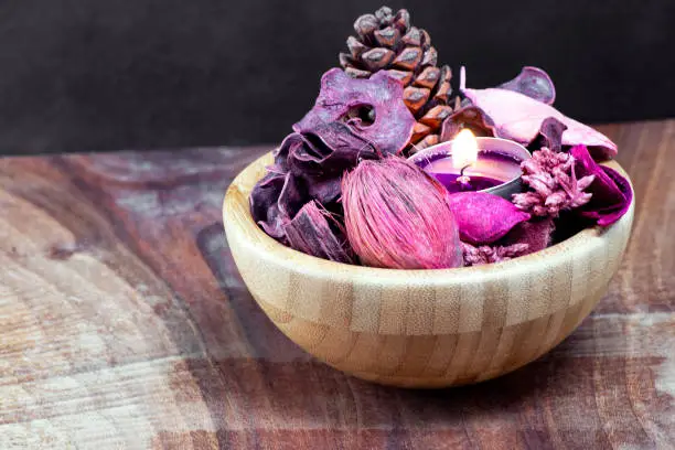 pourple tealight and dry potpourri in a wooden bowl over a table with black background