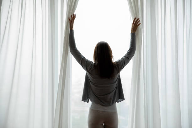 istock Young woman wake up open curtains at home 1218204722