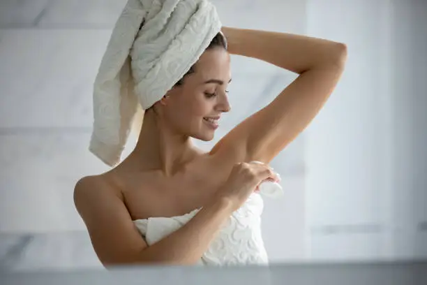 Millennial female wrapped in towel after shower use antiperspirant or deodorant after bath at home, young woman take care of armpit skin do daily beauty treatment in bathroom, hygiene concept