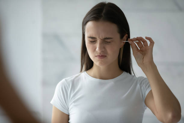 Young woman cleaning ears with cotton stick Young woman stand in bathroom look in mirror clean ears with cotton bud, millennial girl feel pain cleansing using stick or swab after shower in home bath, hygiene, daily routine concept cotton swab stock pictures, royalty-free photos & images