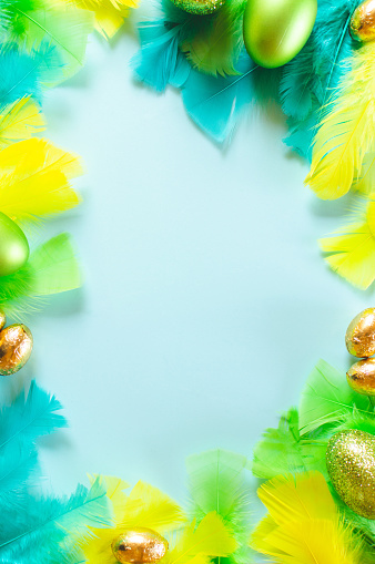 Top down view of a blue background framed by Easter candy eggs and yellow, blue and green feathers