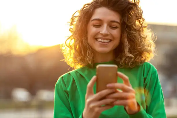 Photo of Young hipster woman using smartphone at sunset