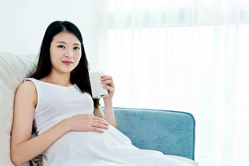 Pregnant woman drinking milk on a sofa