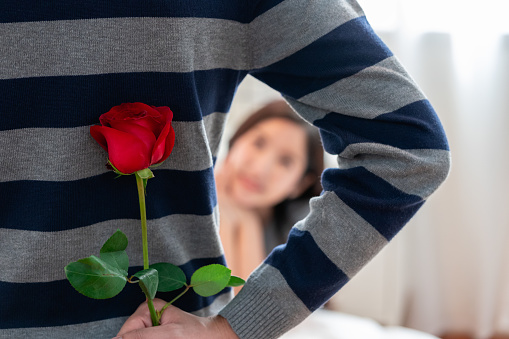 Unexpected moment valentine day, Young Couple in Love and a Man hiding holding surprise red rose behind back for beautiful young woman, happy woman is on blurred background