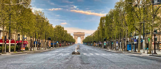Champs-Elysées completely empty during the health crisis Paris, France - April 11, 2020 - View of the avenue des Champs-Elysées completely empty during the confinement linked to the health crisis of the coronas virus. In the foreground, the cobblestones of the avenue covering the road and the first stores located on the sides of the Champs-Elysées are visible. In the background, the Arc de Triomphe under a sunrise is visible. arc de triomphe paris photos stock pictures, royalty-free photos & images